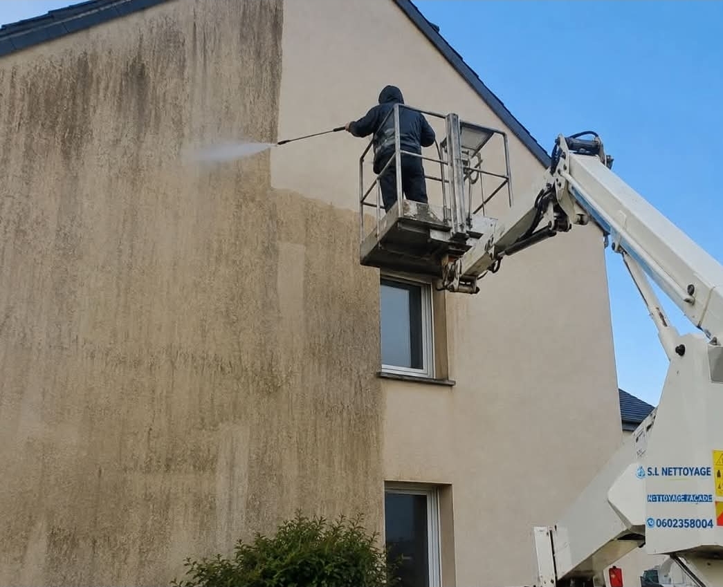 Technicien sur nacelle élévatrice nettoyant une façade au jet haute pression
